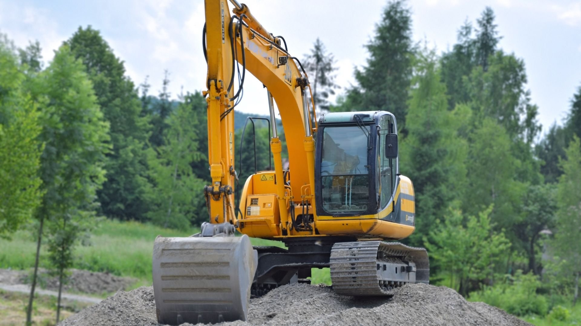 Yellow excavator on dirt pile near forest, ready for construction work