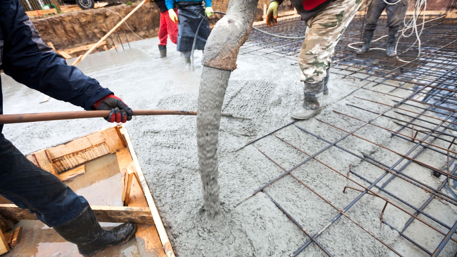 Construction workers pouring concrete over steel reinforcement grid